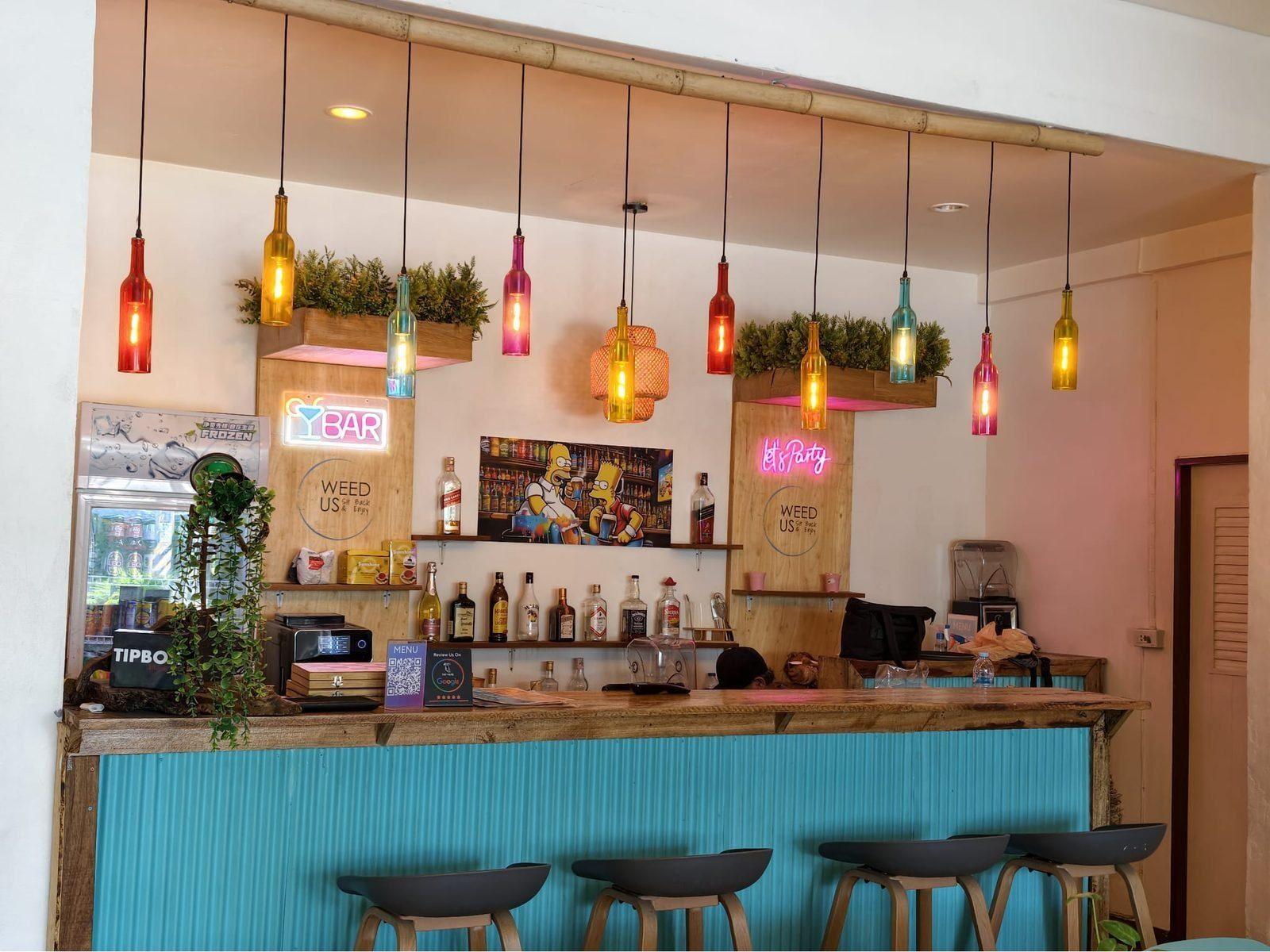 Weed Us — bar counter with hanging lights and neon BAR sign